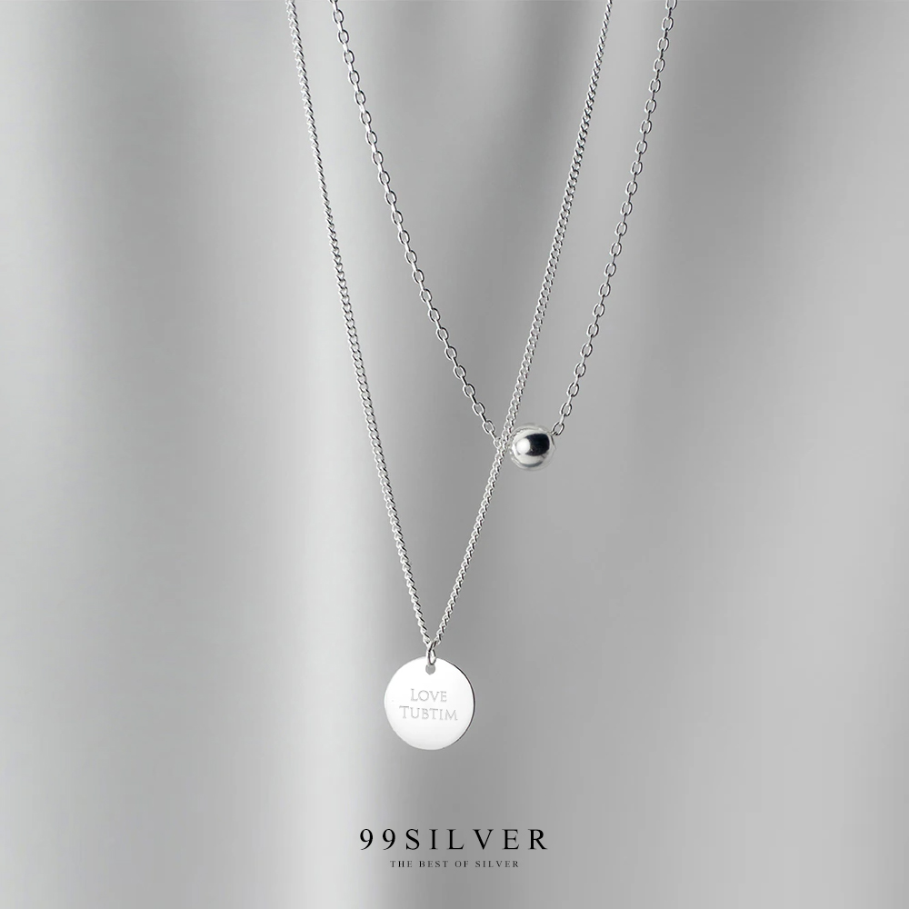จี้เงินแผ่นกลมคล้องอยู่ในสร้อยคอดีไซน์แบบสองชั้นพร้อมชาร์มกลมน่ารัก