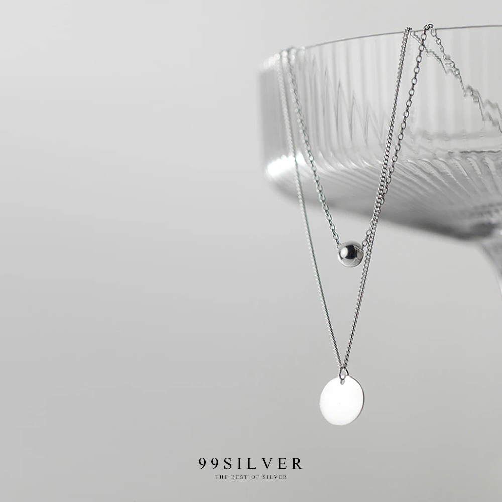 จี้เงินแผ่นกลมคล้องอยู่ในสร้อยคอดีไซน์แบบสองชั้นพร้อมชาร์มกลมน่ารัก
