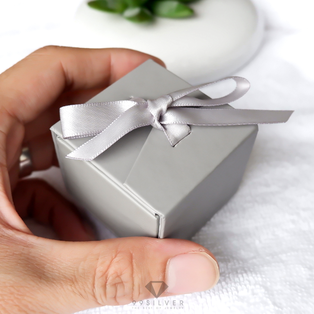 กล่องใส่แหวนสีเทาสี่เหลี่ยม มีริบบิ้นผูกโบว์สำหรับยึดฝา ข้างในบุด้วยสปั้นช์นิ่มสีน้ำตาลเข้ม
